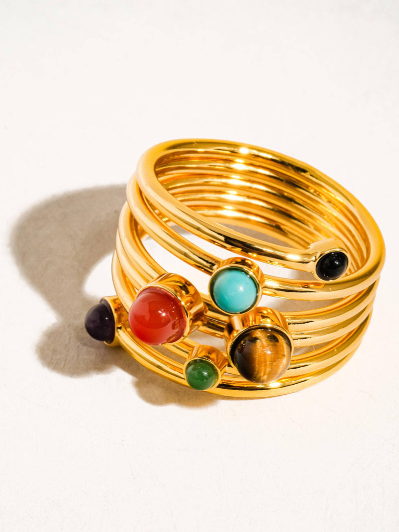 Close-up of a gold statement ring featuring multiple vibrant gemstones, including red, turquoise, green, and purple accents, set in a spiral design