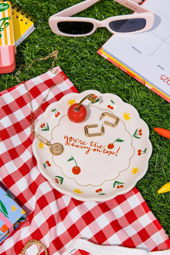 trinket tray with jewelry inside surrounded by accessories on a red gingham tablecloth