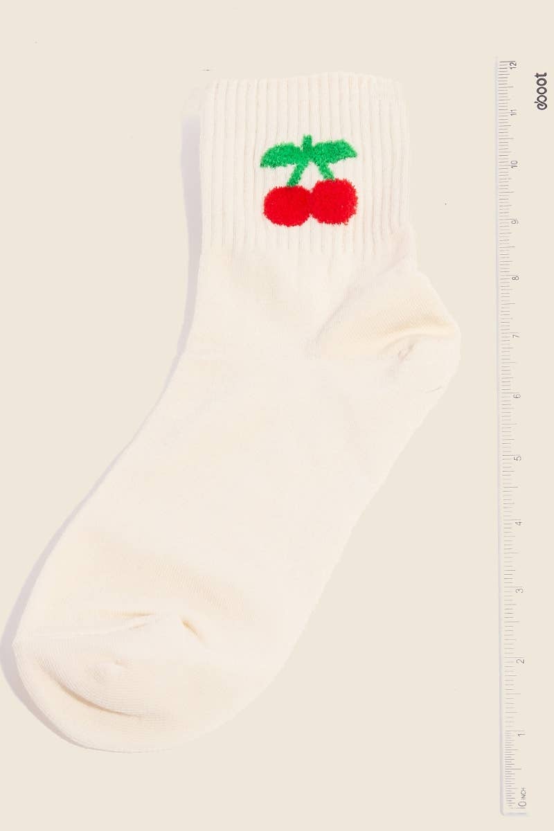 A single beige sock with a vibrant red cherry embroidery featuring green stems, displayed alongside a ruler for size reference.