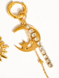 Close-up of a gold crescent moon earring with a star cutout, adorned with rhinestone chains and golden bead accents for a celestial look.