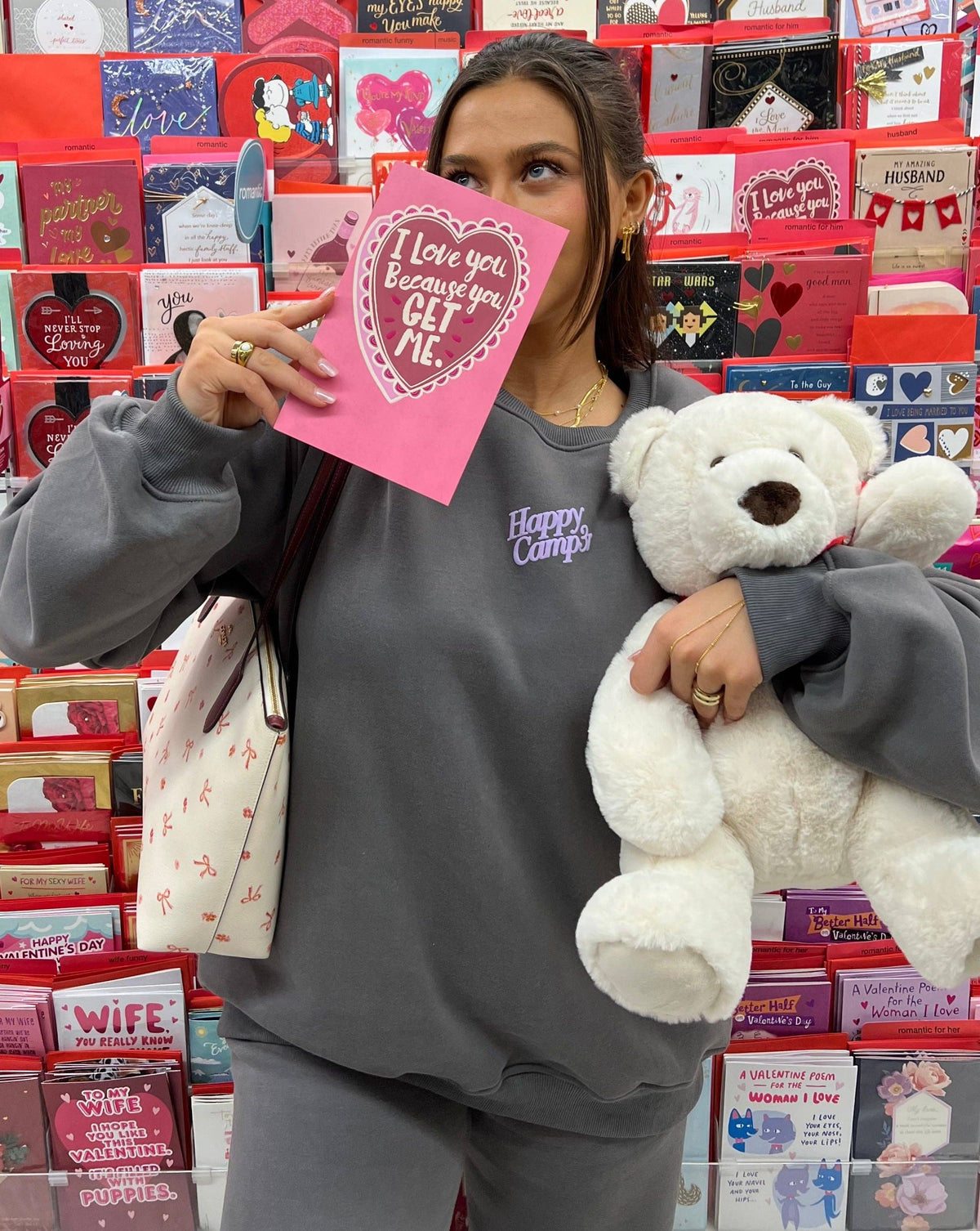 A person wearing the "I'll Always Love You" dark gray fleece sweatshirt, featuring the "Happy Camp3r" lavender puff print logo on the front. Holding a Valentine's Day card and a plush teddy bear, this cozy, oversized sweatshirt is styled for a cute and comfy look.