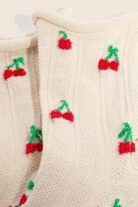 Close-up of intricate cherry embroidery on beige socks showcasing vibrant red cherries with green stems against a textured beige background.