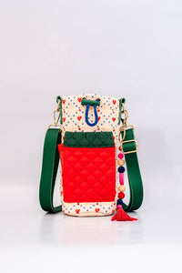 Colorful quilted water bottle sling with cherry print, green adjustable strap, red front pocket, and a playful beaded charm with a tassel detail.