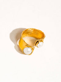 Top view of a gold cuff ring featuring a hammered finish and two pearl embellishments set in square frames