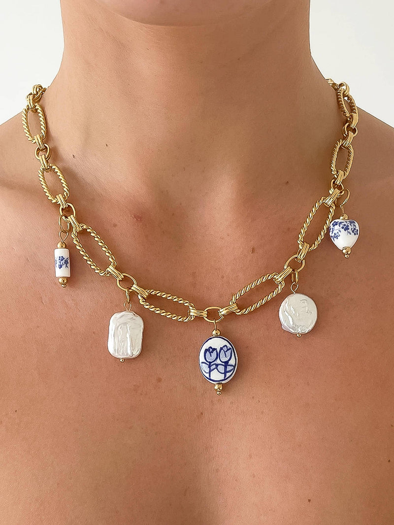 Model wearing a gold chain necklace adorned with blue and white ceramic charms, including tulip and floral designs, for a chic, artistic look