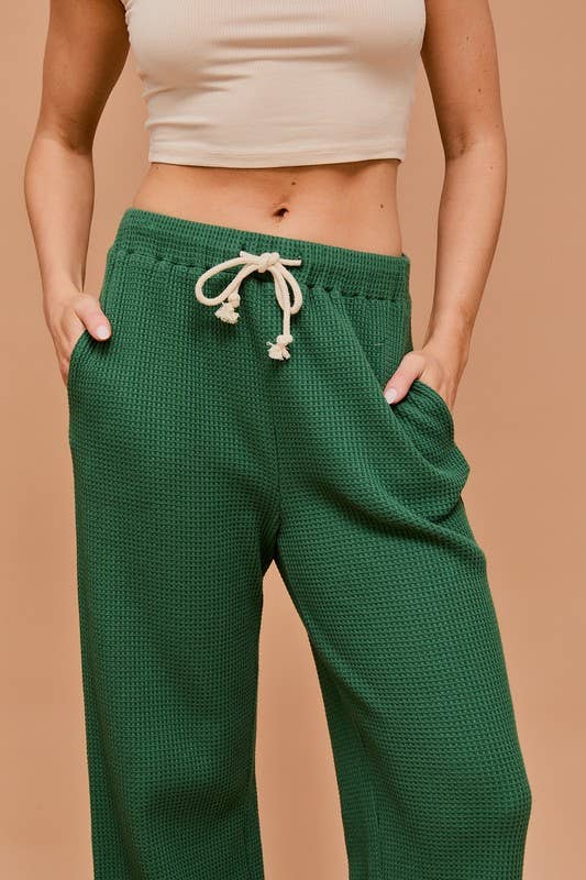 A front view of the model wearing green waffle-knit pants with hands in the pockets, highlighting the textured fabric and drawstring waist.