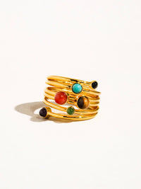 Side view of a gold spiral ring with colorful gemstones in red, turquoise, green, black, and purple hues, offering a bold and artistic look