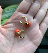 Close-up of tomato hoop earrings resting on an open palm, showcasing their size and gold-tone details.