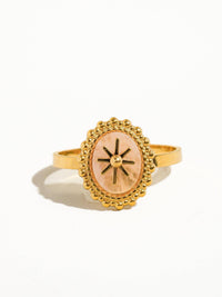 Front view of a gold ring featuring a pink marbled oval stone with a starburst design, framed by intricate beaded details."