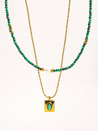 Close-up of a gold chain necklace with a rectangular pendant holding a green stone, paired with a green beaded layer and pearl accents