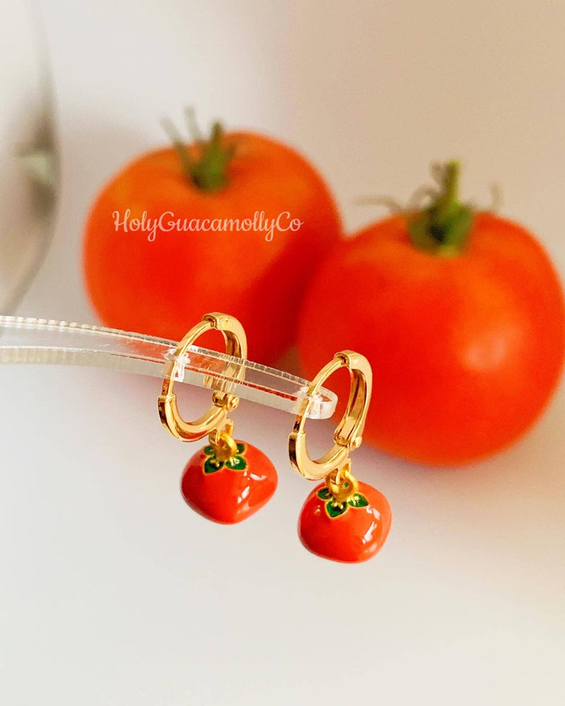 Tomato hoop earrings displayed in front of fresh cherry tomatoes, highlighting their fun and food-inspired design.