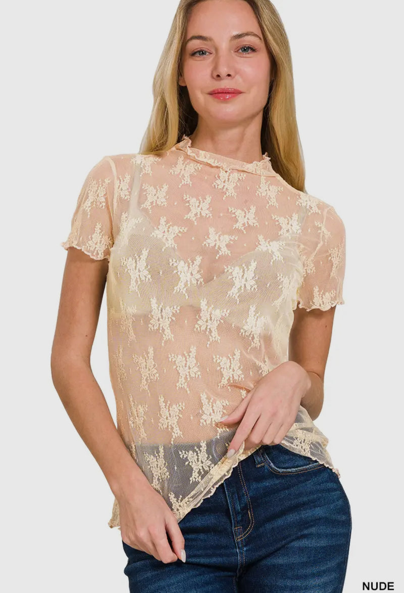 Model wearing a nude lace top with floral patterns, short sleeves, and a high neckline, paired with denim jeans for a chic, casual look