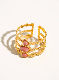 A front-facing close-up of a triple-band gold ring with pink gemstone accents, showcasing its elegant and sophisticated design