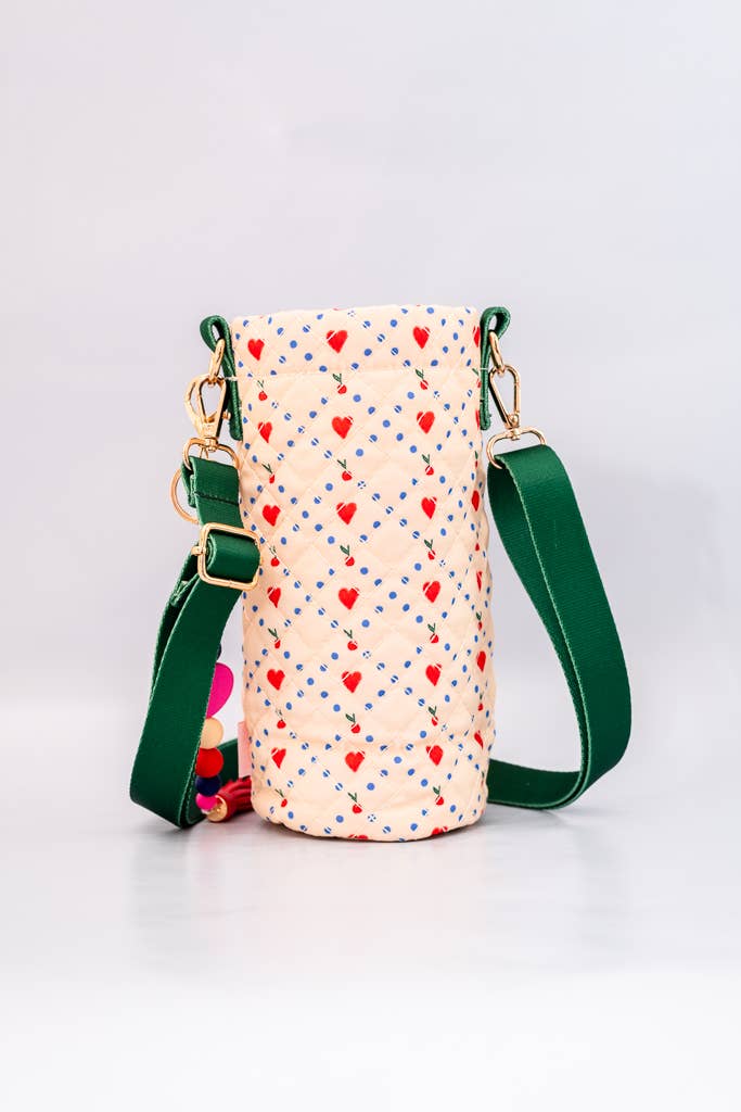 Colorful quilted water bottle sling with cherry print, green adjustable strap, red front pocket, and a playful beaded charm with a tassel detail with back view with hearts and quilted pattern 