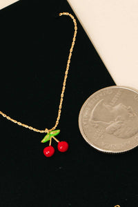 Close-up view of the Gold Dipped Epoxy Cherry Pendant Necklace next to a quarter for scale, emphasizing the intricate design of the cherry charm.