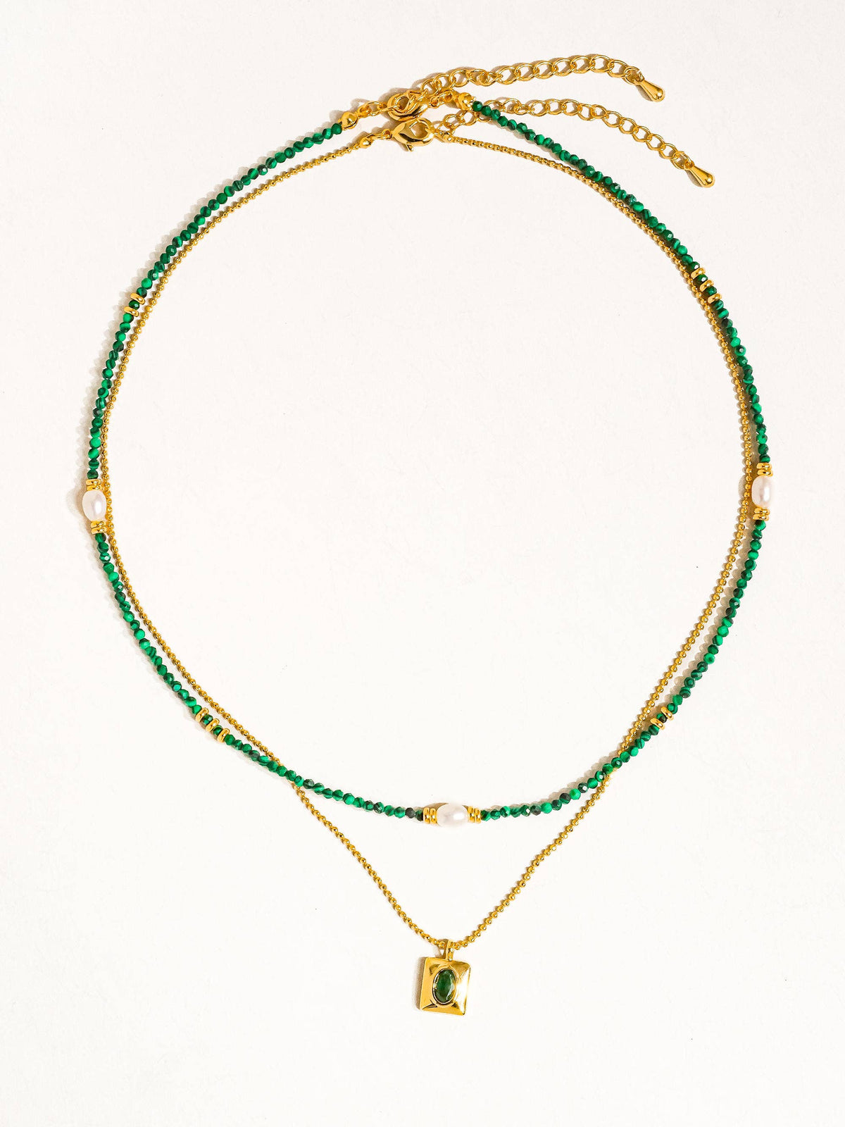 Detailed view of the layered necklace showing green beads, a pearl accent, and a gold chain with a rectangular green-stone pendant.