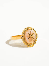 Side view of a gold ring featuring a pink oval stone with a starburst design, framed by intricate beaded detailing for an elegant finish