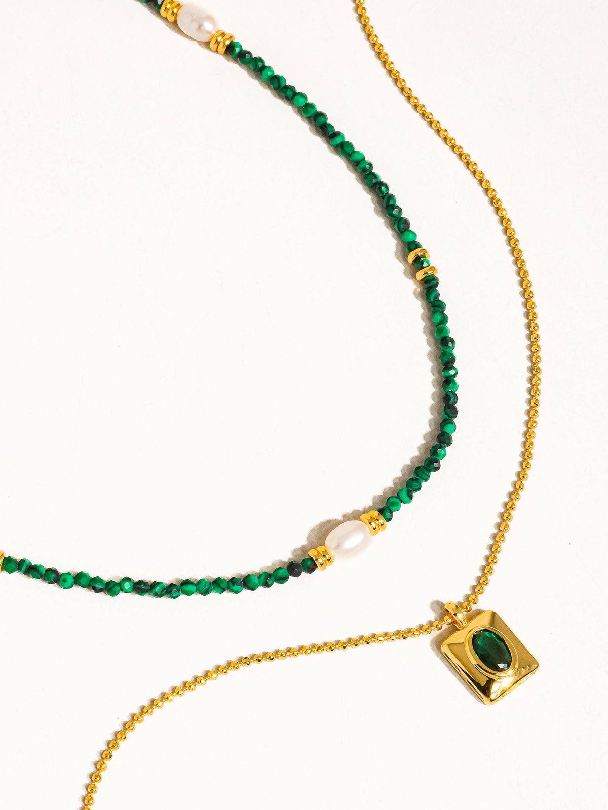 Full view of a layered green and gold necklace with pearl accents and a rectangular gold pendant featuring a green stone, laid flat.