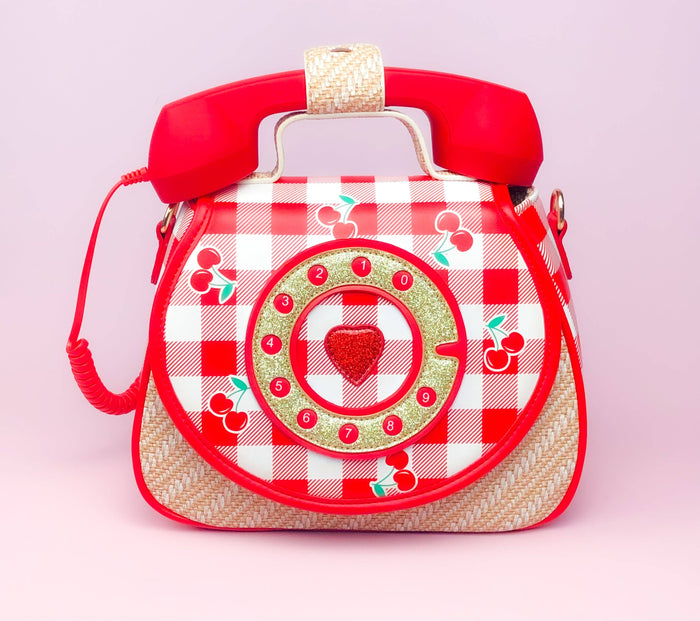 Retro cherry picnic phone purse with red gingham print, rotary dial design, and faux telephone handle on a pink background.