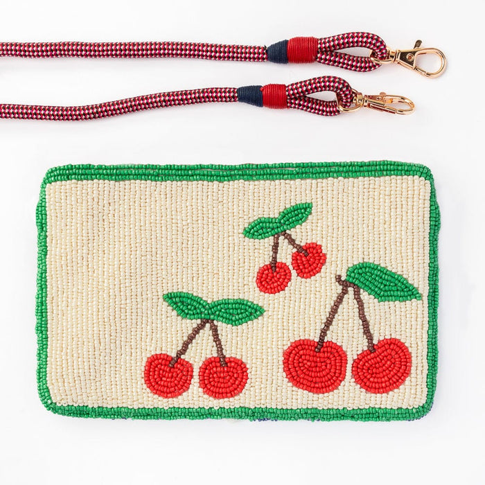  A hand-beaded clutch with a cream background featuring vibrant red cherries and green leaves, framed by a green beaded border. Includes a detachable red and navy woven strap with gold hardware.