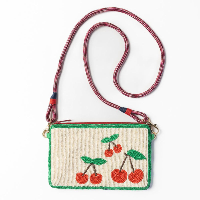 The full view of the Leila Cherries Clutch with its detachable red and navy rope strap, showcasing the playful cherry motif on the front and gold clasp attachments.